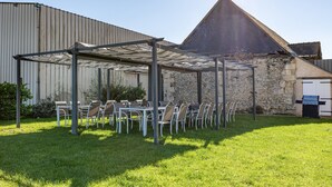 Un espace extérieur abrité, avec des tables et des chaises, un bâtiment en pierre et une structure métallique en arrière-plan.