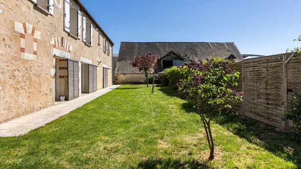 Une cour avec un bâtiment en pierre, une clôture en bois et un petit arbre.