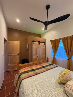 Ein Schlafzimmer mit Bett, Deckenventilator, Kleiderschrank und einem Fenster mit Vorhängen.
