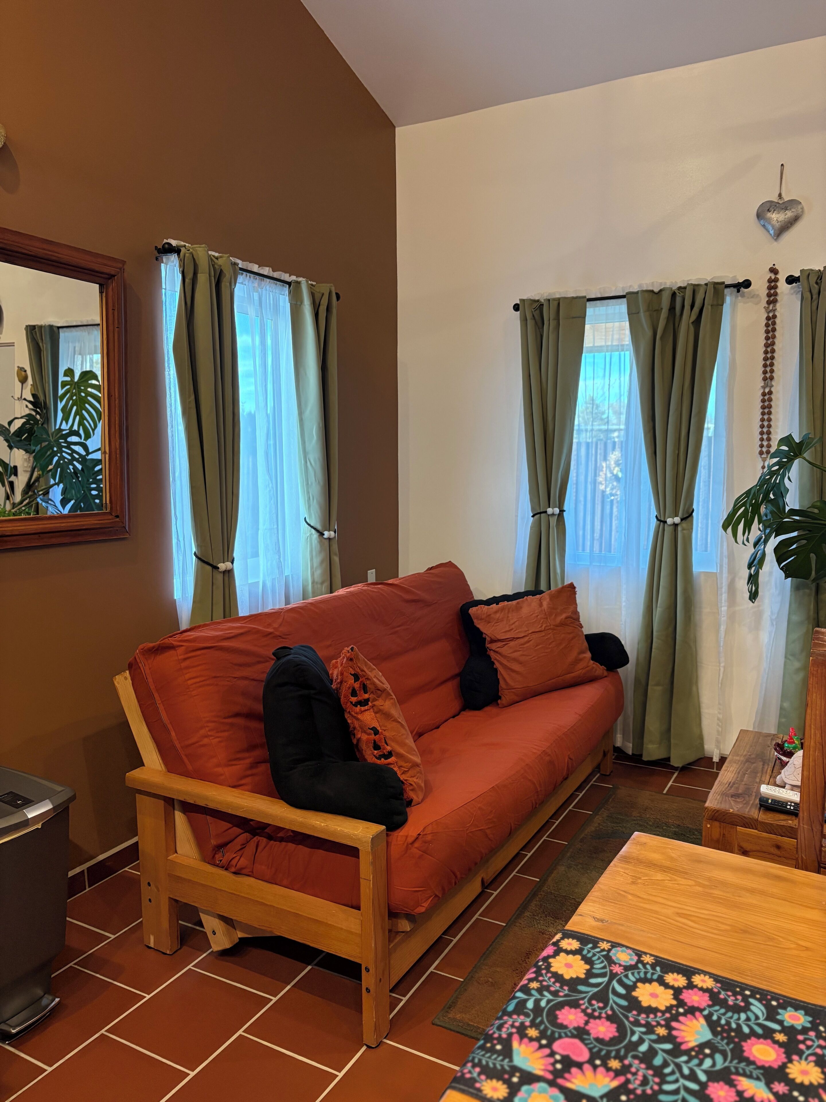 Ein gemütliches Wohnzimmer mit einer Holzsofa, grünen Vorhängen und einem Fliesenboden.