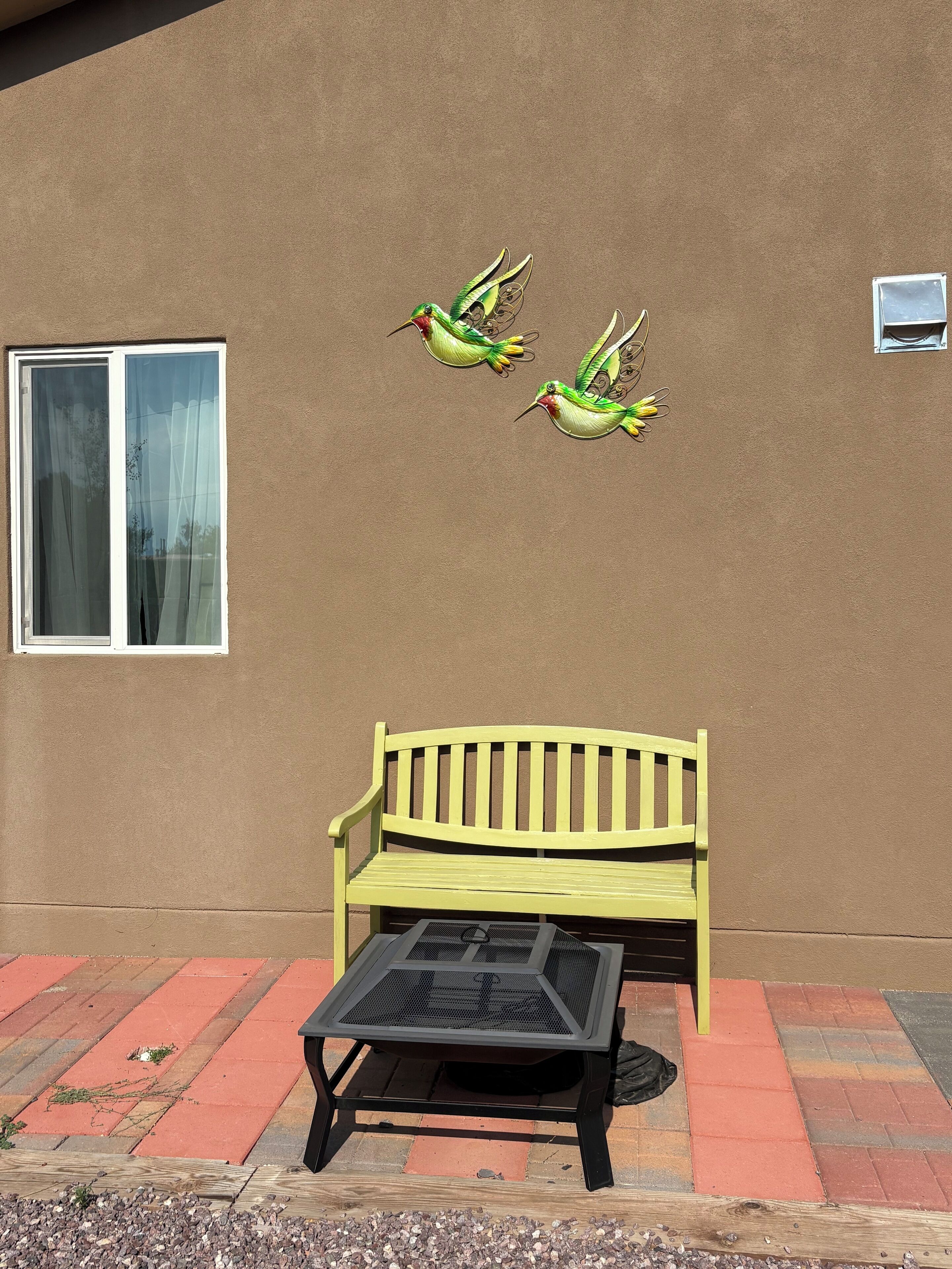 A bench with a mesh table in front, a wall with a window, and three birds painted on the wall.