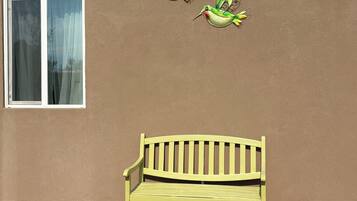 A bench with a mesh table in front, a wall with a window, and three birds painted on the wall.
