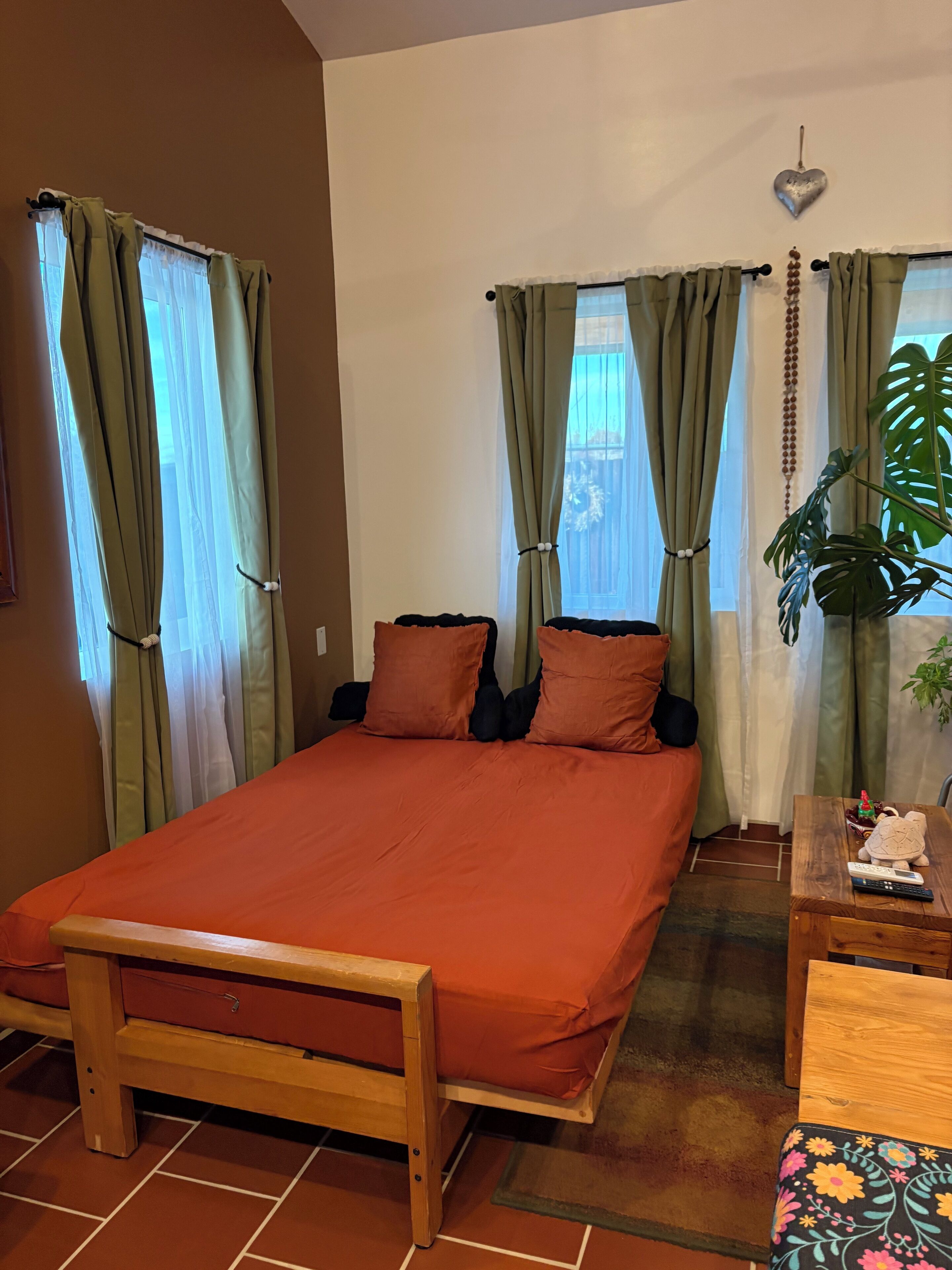Een slaapkamer met een houten bed, groene gordijnen, een nachtkastje van hout en een potplant.