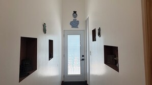 A narrow hallway with white walls, a door at the end, and a small window above it.