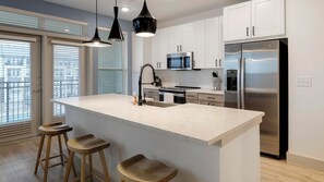 A modern kitchen with a central island, stainless steel appliances, and wooden stools. - Landing | Stylish 2BD, Clubhouse, Gym (Garland)