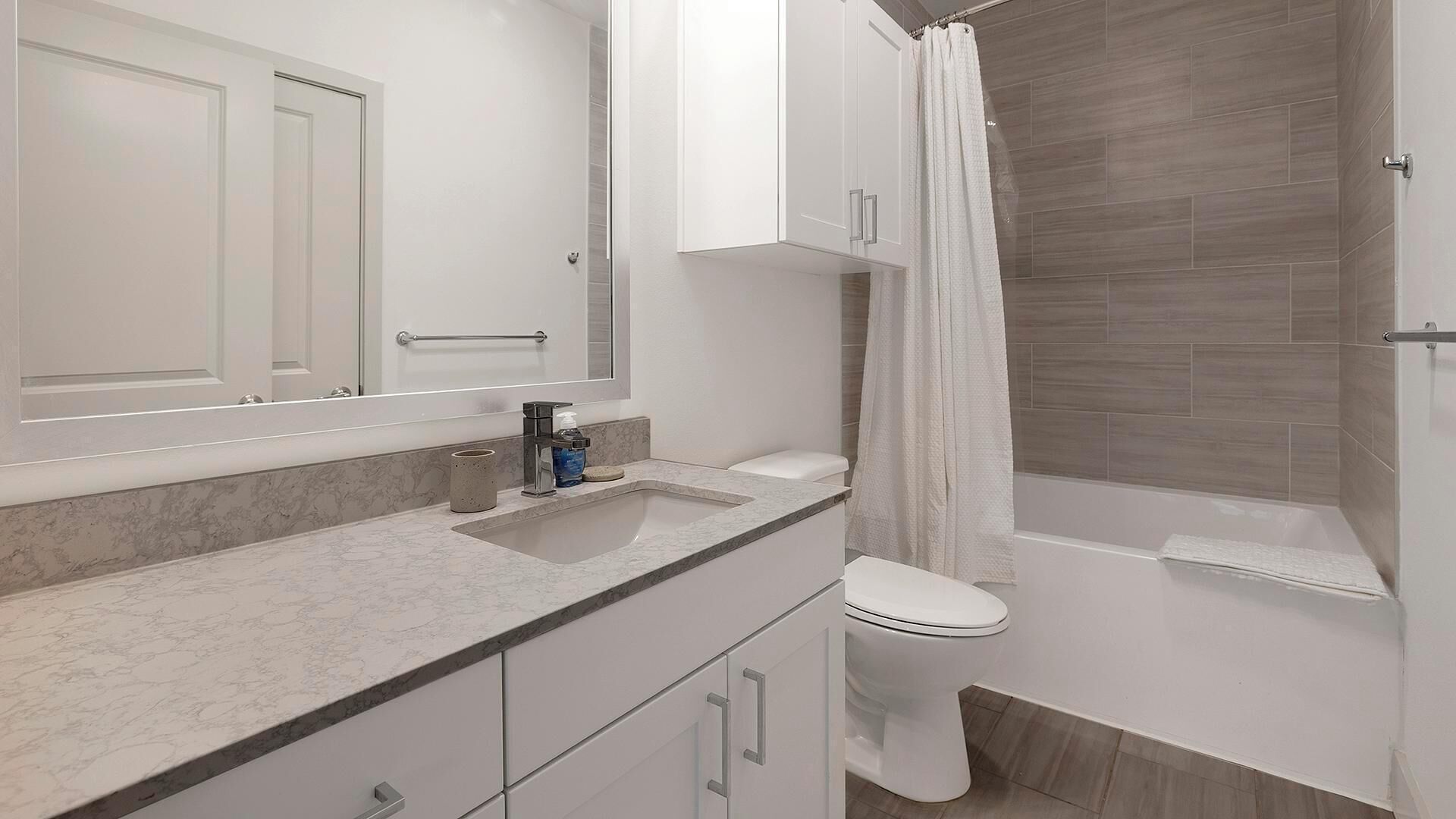 Et moderne badeværelse med bordplade i marmor, et hvidt toilet og en bruser med gardin.