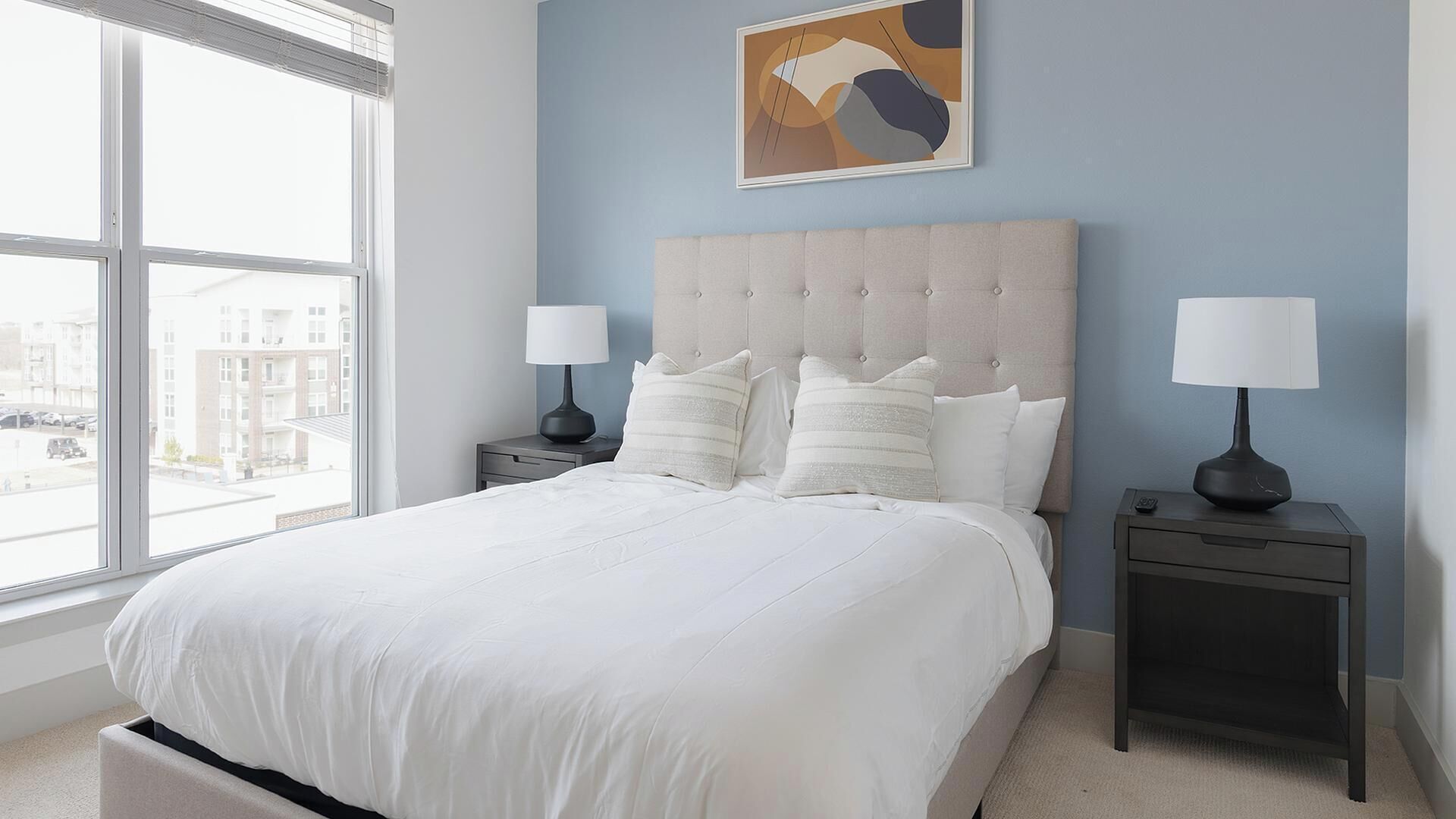 A bedroom with a large bed, two bedside tables, and a window with a view of buildings.