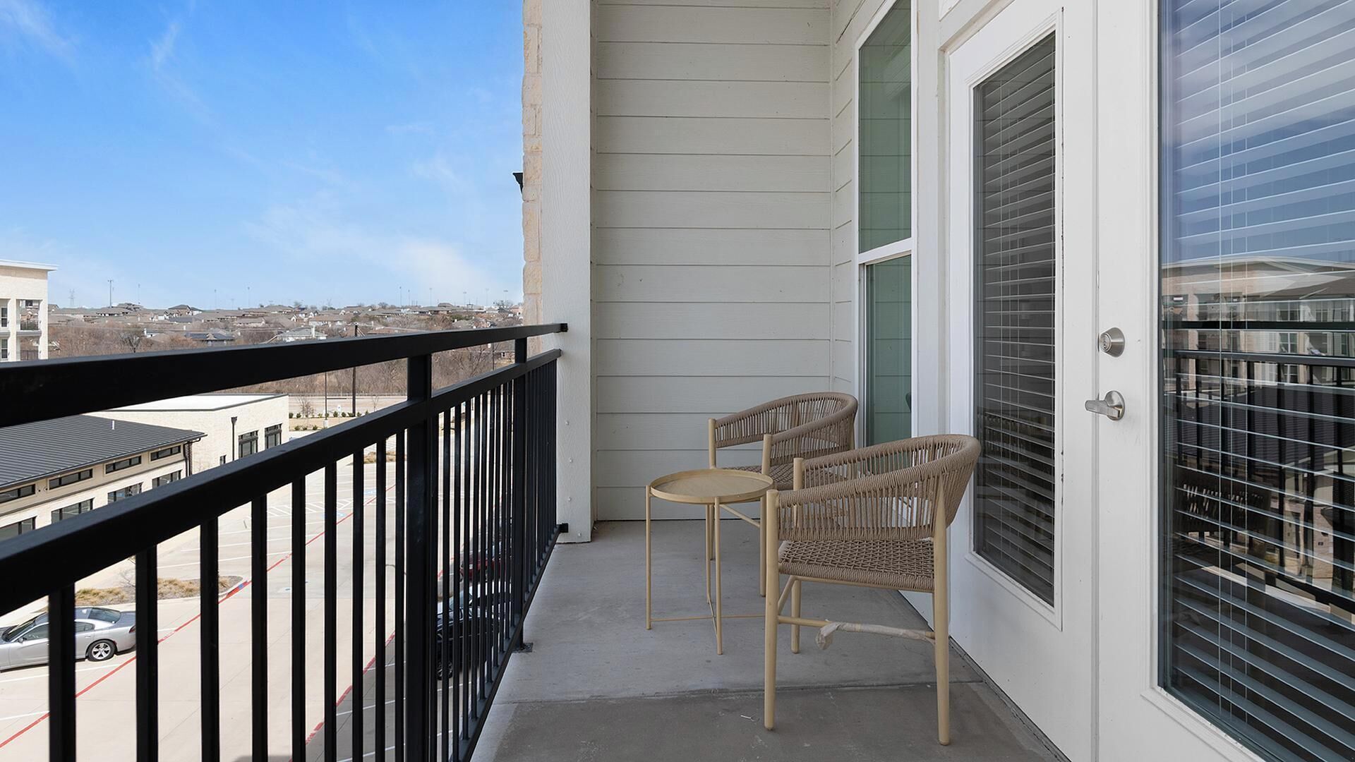 A balcony with two wicker chairs and a door with blinds.