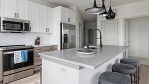 A modern kitchen with white cabinets, stainless steel appliances, a marble countertop, and a central island with bar stools.