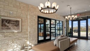 A lobby with stone walls, a large chandelier, a sofa, and a glass door leading outside.