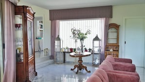 A spacious living room with a marble floor, a pink sofa, a wooden cabinet, and a dining table with a vase of flowers. - Villa Letizia (Chieti)