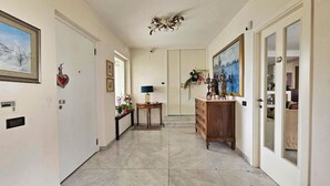 A hallway with a marble floor, a wooden dresser with a mirror, a chandelier, and framed artwork on the walls. - Villa Letizia (Chieti)