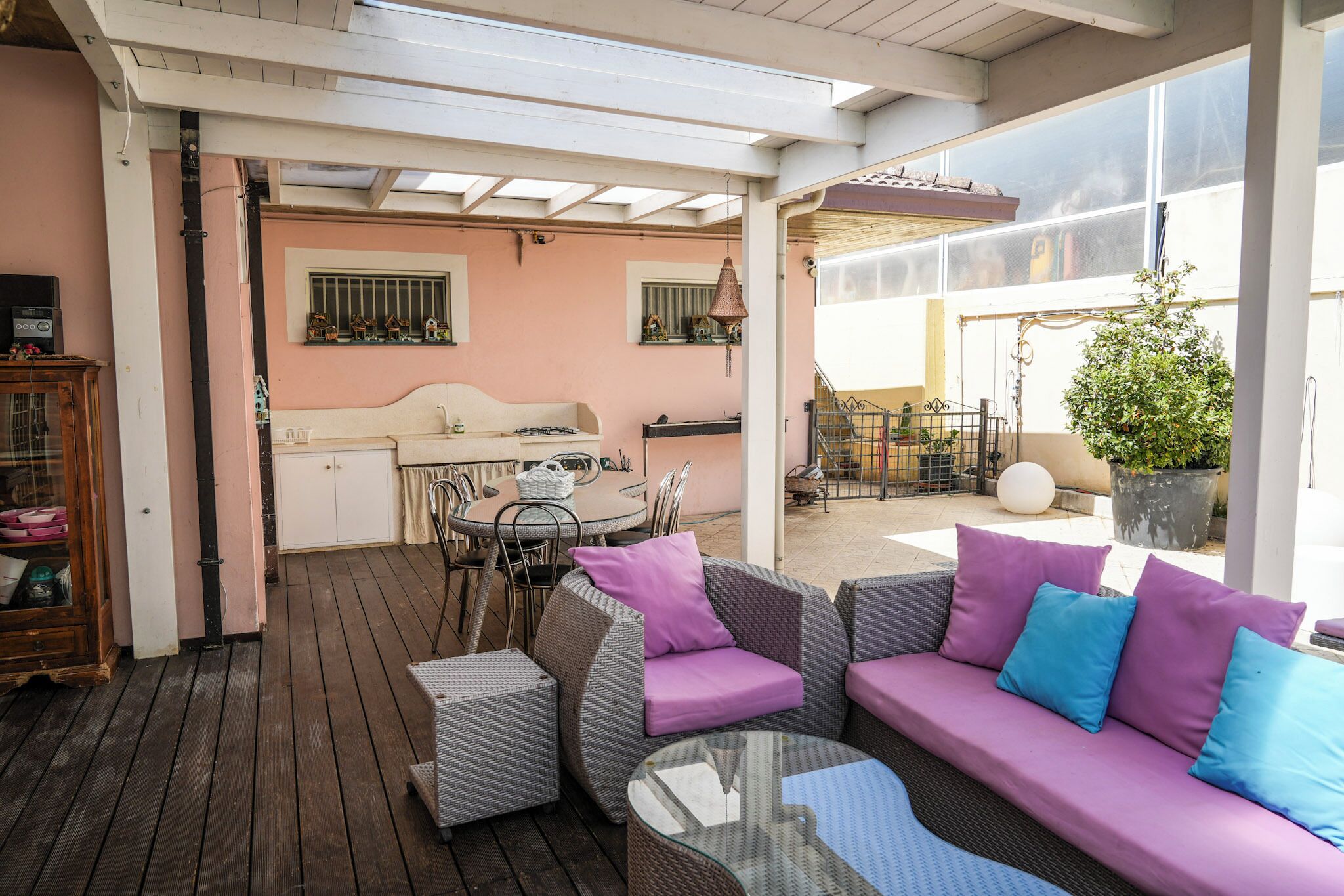 A covered patio area with wicker furniture, a dining table, and a kitchen area visible through an open door.