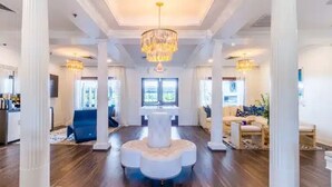 A spacious living room with a central white circular seating area, high ceilings, and large windows. - Landing | Spectacular 2BD, Game Room, Courtyard (Gulf Shores)