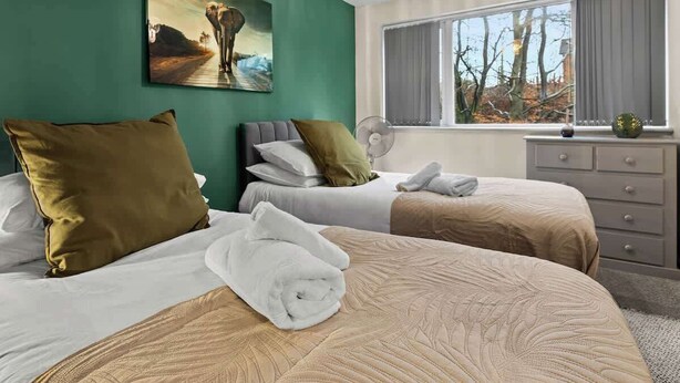 Ett hotellrum med två sängar, ett stort fönster med utsikt över träd, en tavla på väggen och en byrå med lådor.