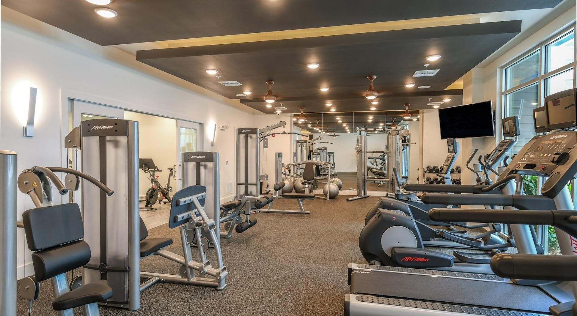 Un gimnàs amb equip de cardio, aparells de musculació i un mirall.