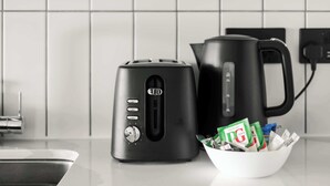 Ett kök med en svart brödrost, en svart kaffebryggare och en vit skål som innehåller påsar med PG-produkten.