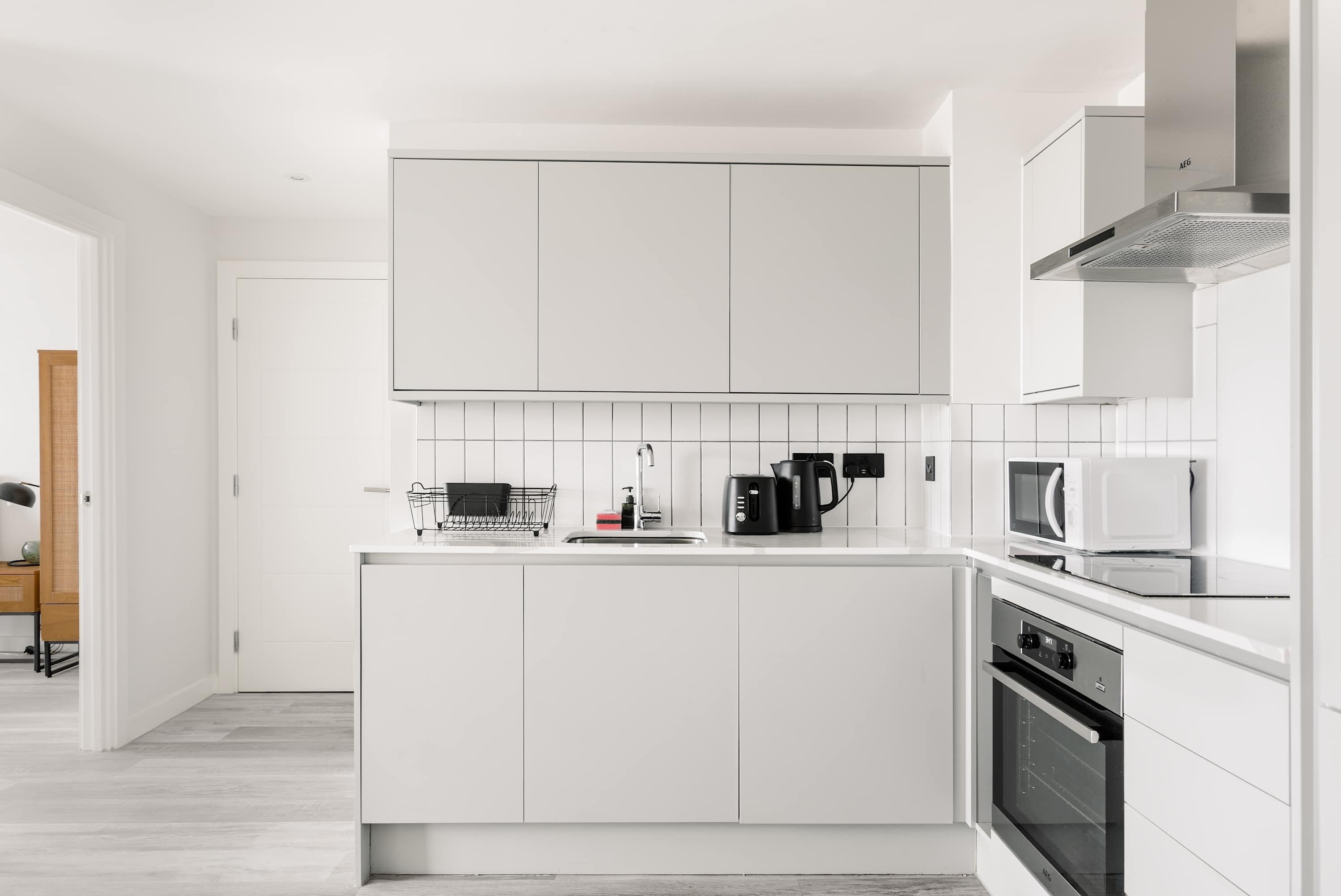 A modern kitchen with white cabinetry, a stainless steel range hood, a microwave, and a built-in oven.