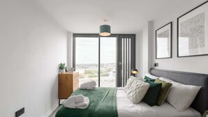 Ein modernes Schlafzimmer mit einem großen Bett, Blick durch eine Schiebetür, einem Nachttisch mit Lampe und gerahmten Kunstwerken an der Wand.