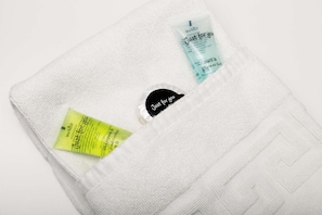 A white towel with three toiletries: a yellow shampoo conditioner, a blue shower gel, and a black bar of soap. - Modern Central Birmingham 2 Bed Apartment (Birmingham)