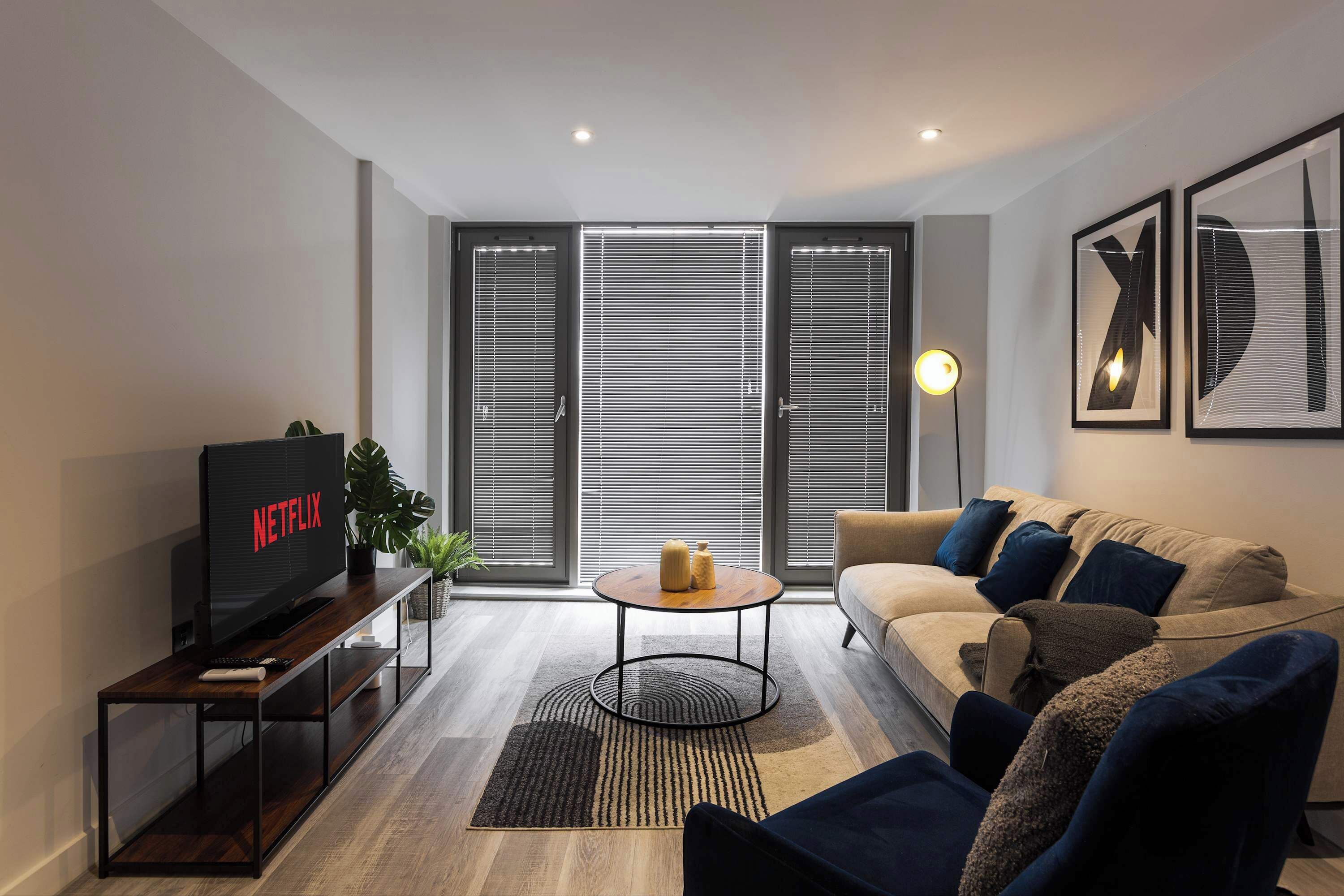 A modern living room with a TV, sofa, coffee table, and blinds.