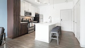 Een moderne keuken met een centraal eiland, roestvrijstalen apparatuur en een wand bekleed met donker hout.