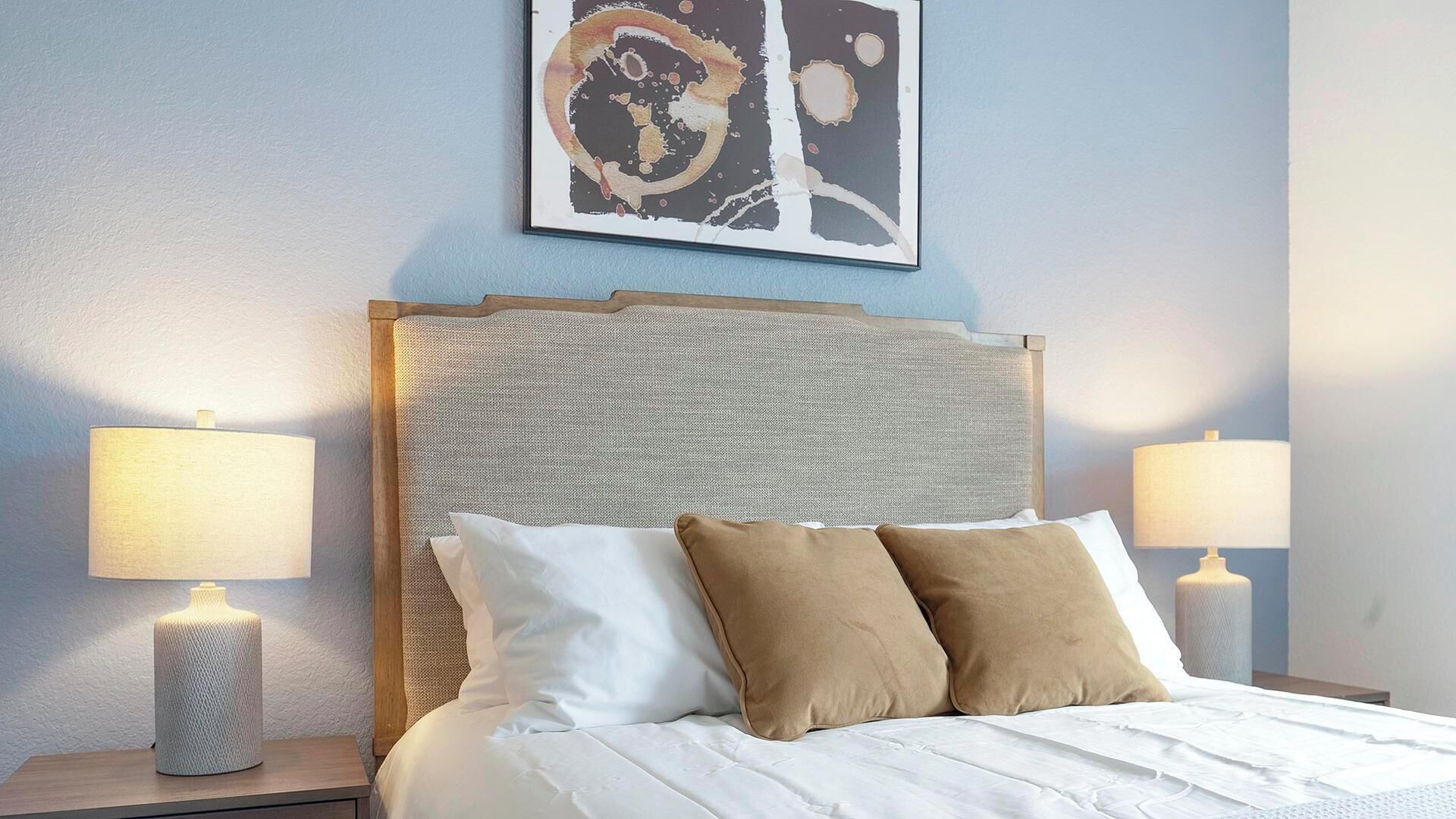 A neatly made bed with white and brown pillows, two bedside lamps, and a textured headboard.
