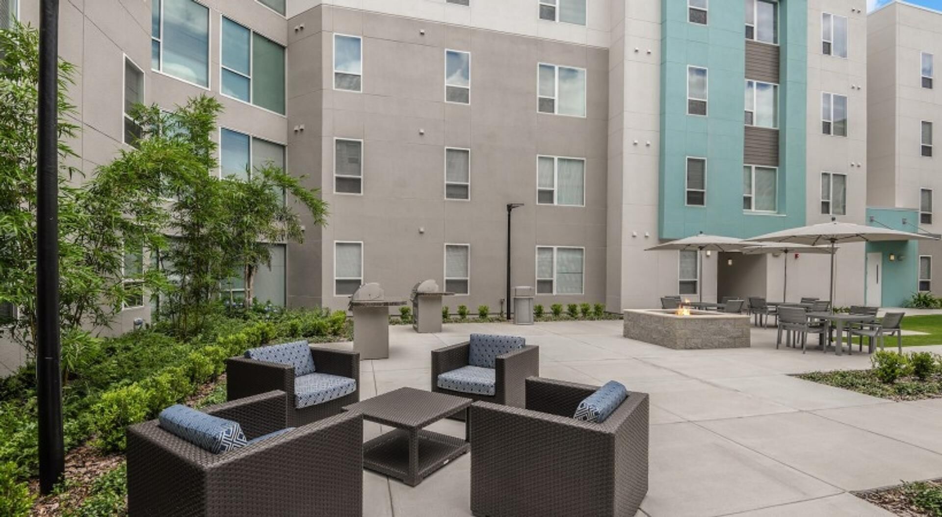 A courtyard with outdoor seating, a fire pit, and a building with multiple windows and balconies.
