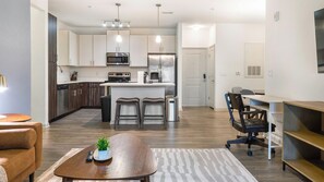 A modern kitchen with stainless steel appliances, a central island with bar stools, and a dining area with a table and chairs.
