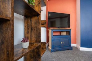 A room with a TV on a wooden stand, a blue cabinet, and a plant on a shelf.