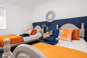A hotel room with two beds, each with an orange blanket, white headboards, and a nightstand with a lamp.