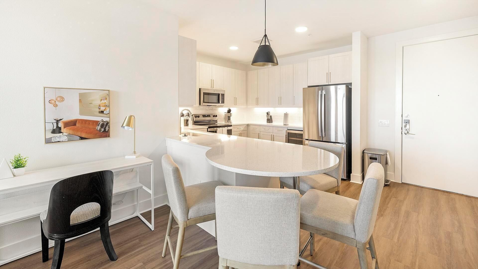 A modern kitchen with white cabinets, stainless steel appliances, and a round dining table with chairs.