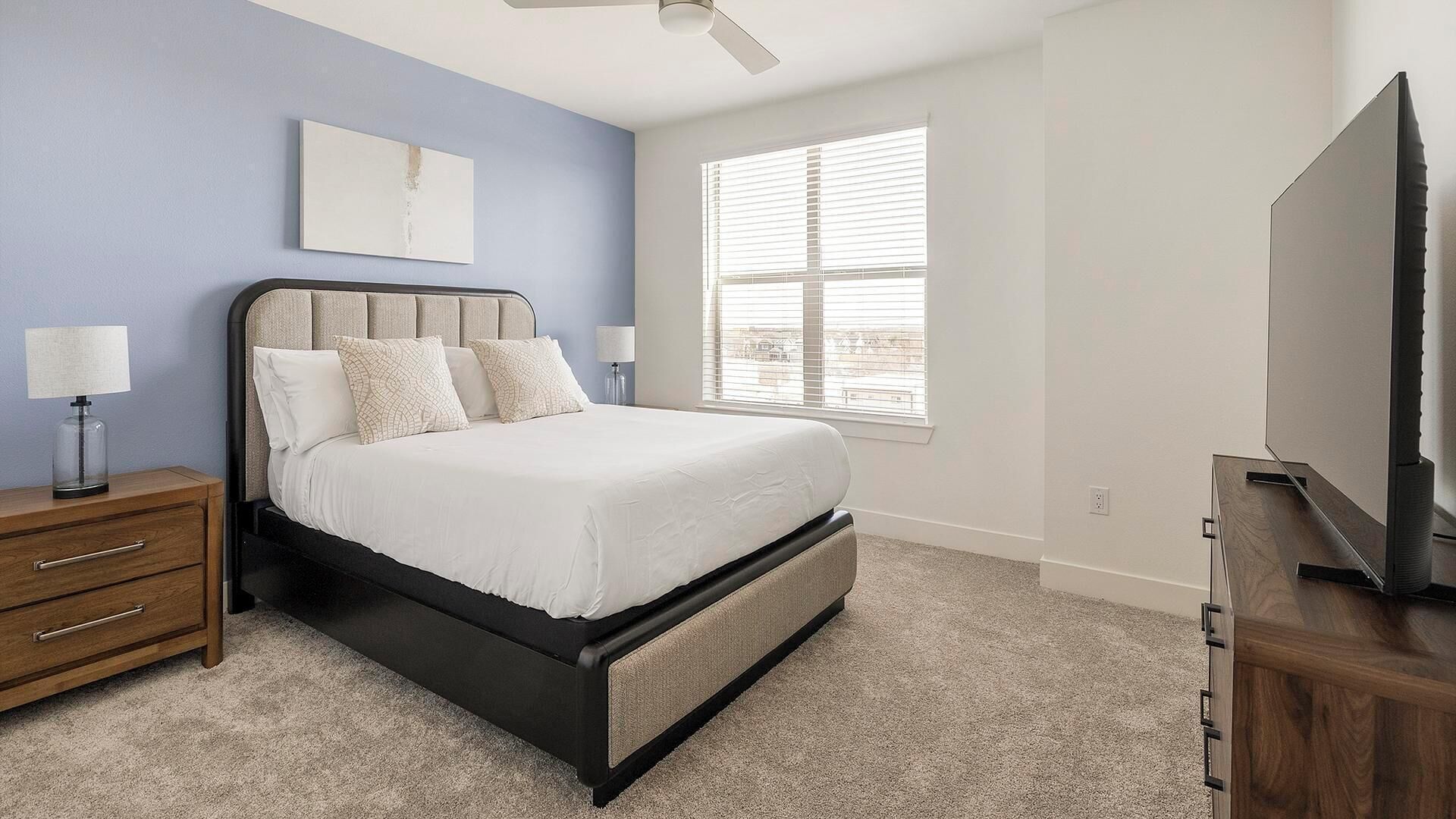 A bedroom with a bed, nightstand, lamp, and a TV.