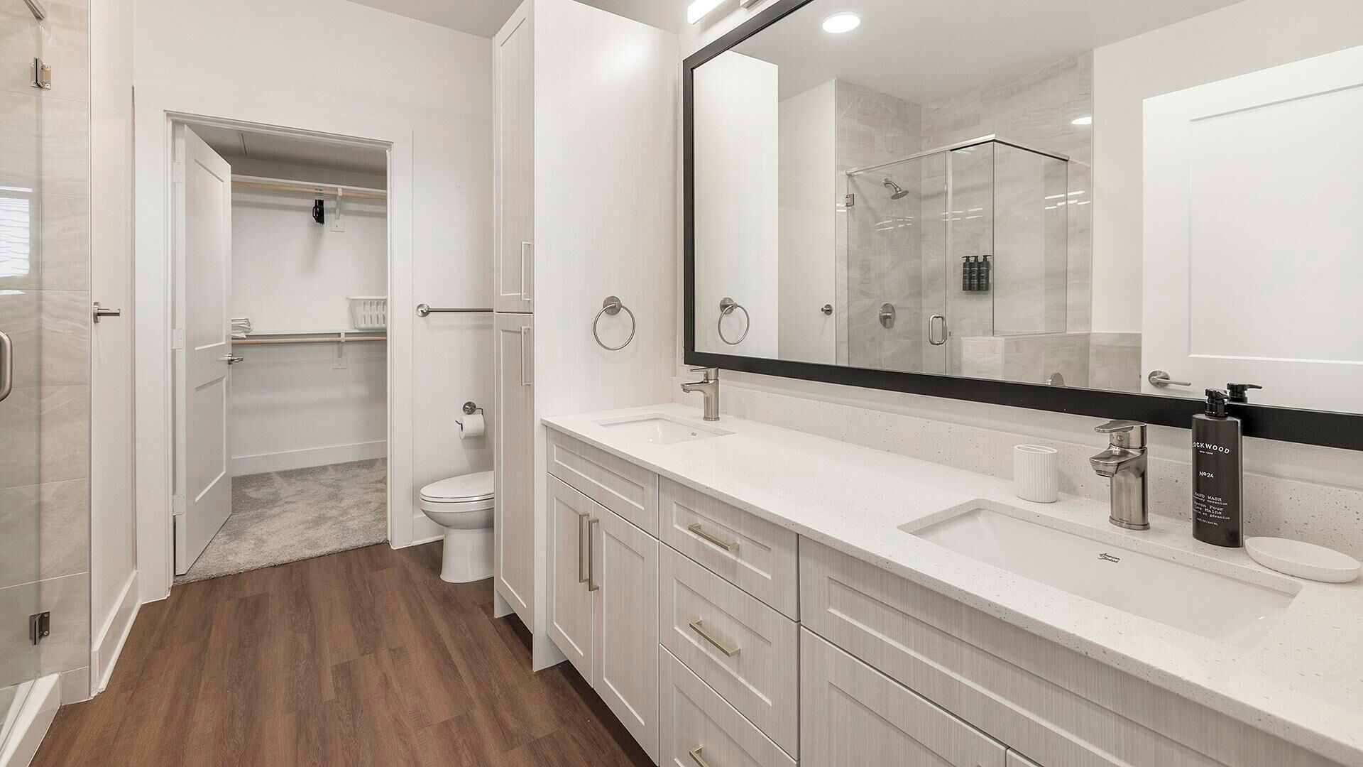 A modern bathroom with a walk-in shower, a large mirror, and a vanity with a sink and storage drawers.
