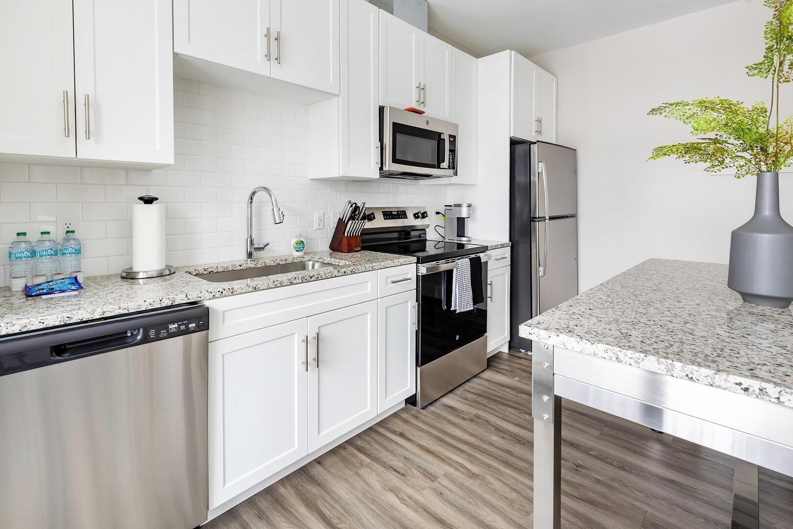 A modern kitchen with white cabinets, a stainless steel refrigerator, a microwave, and a dishwasher.