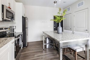 A modern kitchen with white cabinetry, stainless steel appliances, a granite countertop, and a dining area with a table and chairs. - Landing | Modern 1BD, Clubhouse, Courtyard (Cleveland)