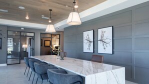 A modern kitchen with a marble island, grey chairs, pendant lights, and framed artwork on the wall.