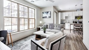 Eine moderne Wohnung mit Wohnzimmer, Essbereich und Küche. Sie verfügt über große Fenster, einen Deckenventilator und Blick auf die Stadt.