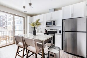 A modern kitchen with white cabinets, stainless steel appliances, a granite countertop, and a dining area with chairs and a vase of flowers. - Landing | Stunning 1BD, Courtyard, Gym (Cleveland)