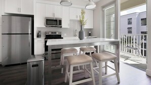 Una cocina moderna con armarios blancos, electrodomésticos de acero inoxidable y una zona de asientos con taburetes de bar.
