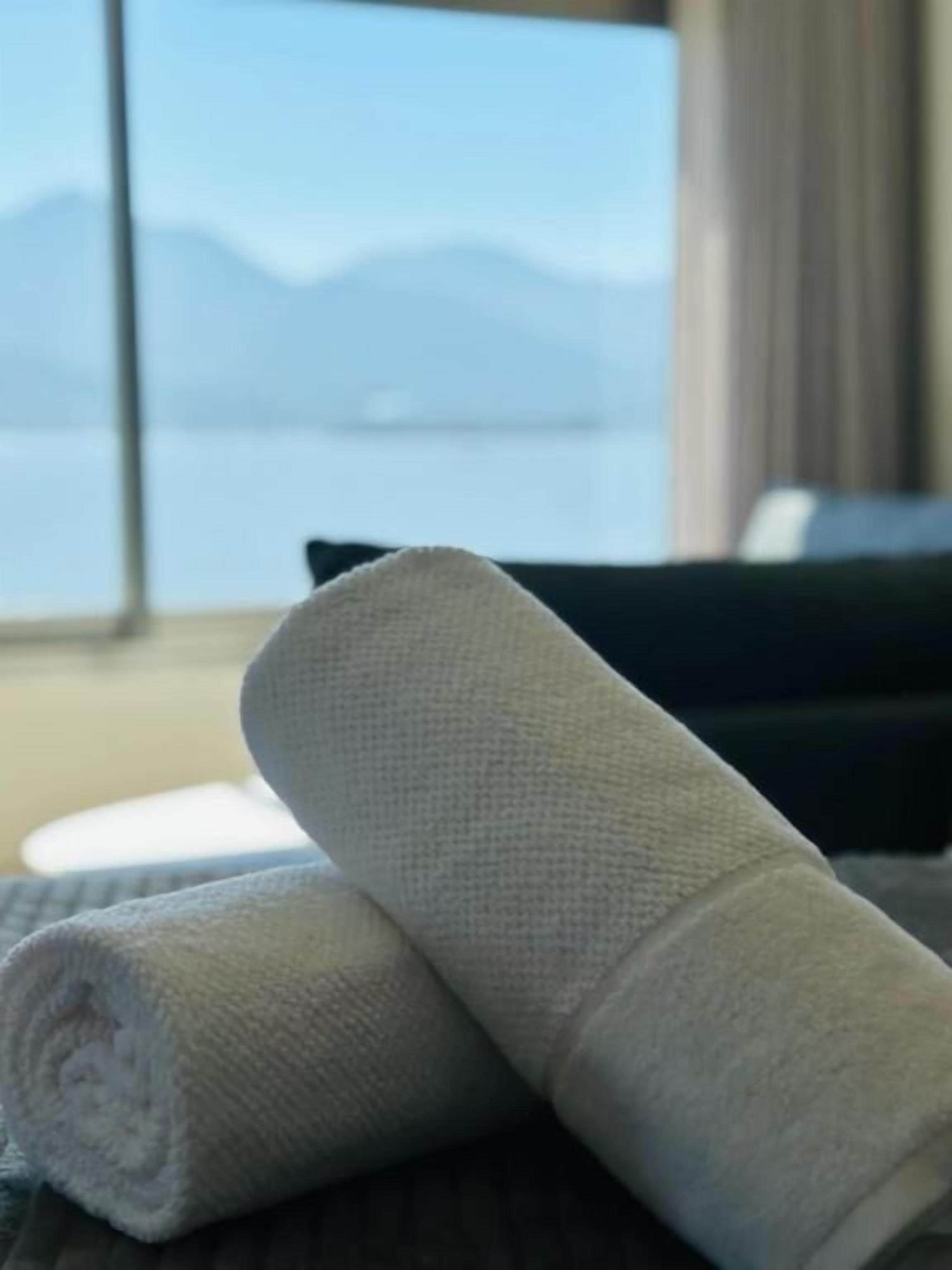 Ein ordentlich gefaltetes weißes Handtuch auf einem Bett mit Blick auf Berge durch ein Fenster.