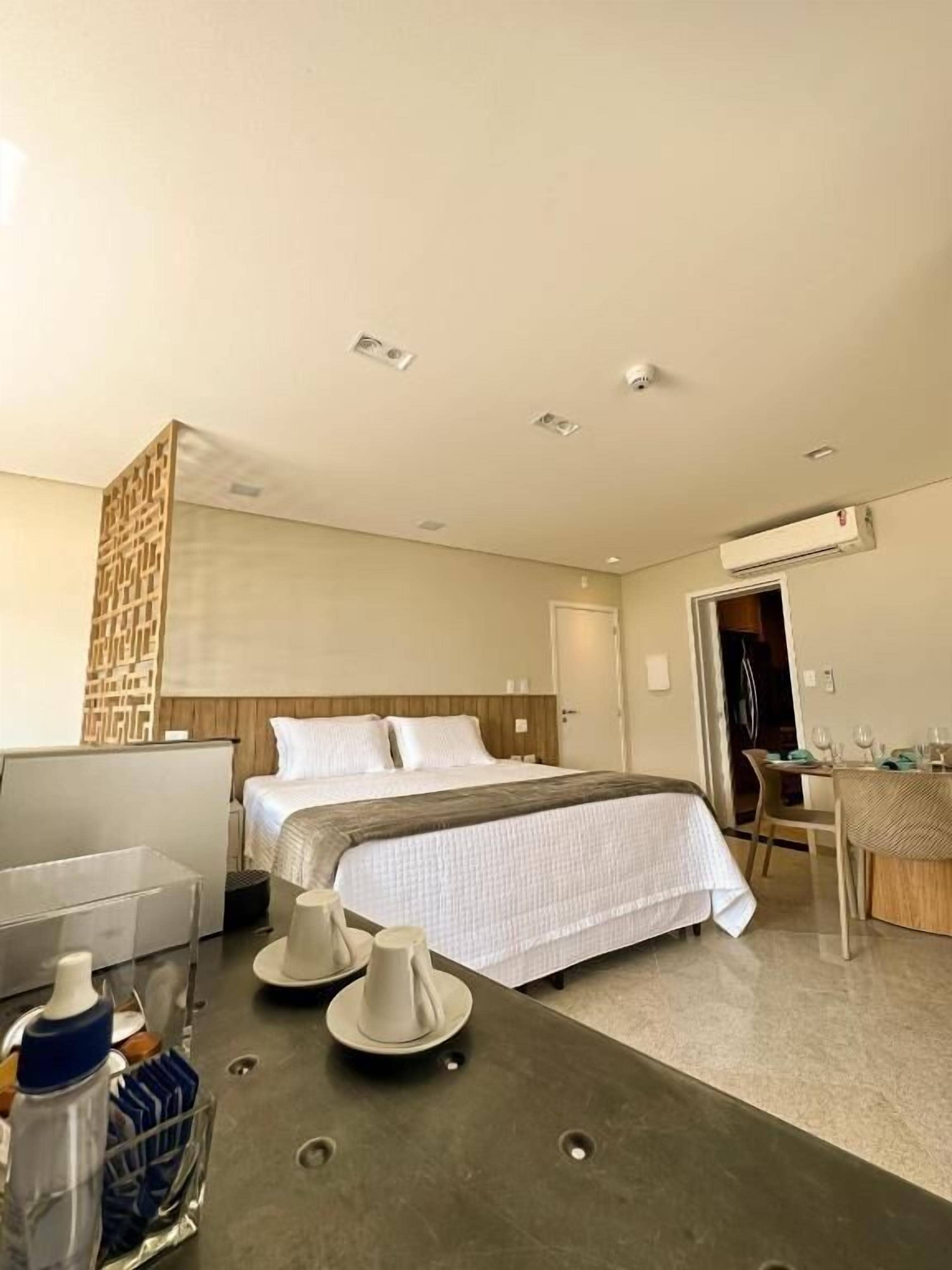 Habitación de hotel moderna con una cama grande, un escritorio con silla, una pequeña mesa con silla y una zona de comedor con mesa y sillas.