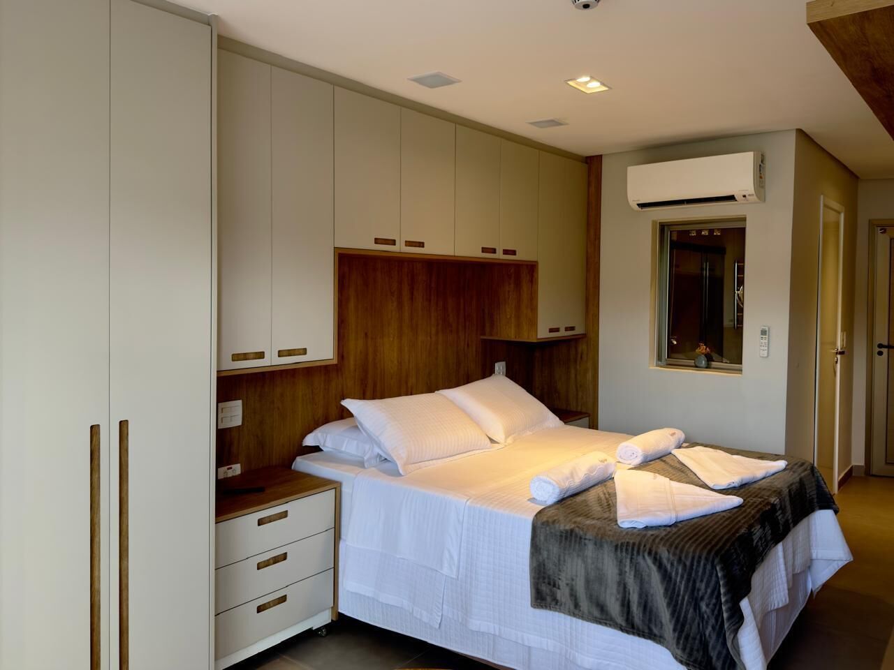 A neatly arranged bedroom with a bed, bedside tables, a wardrobe, and an air conditioning unit.