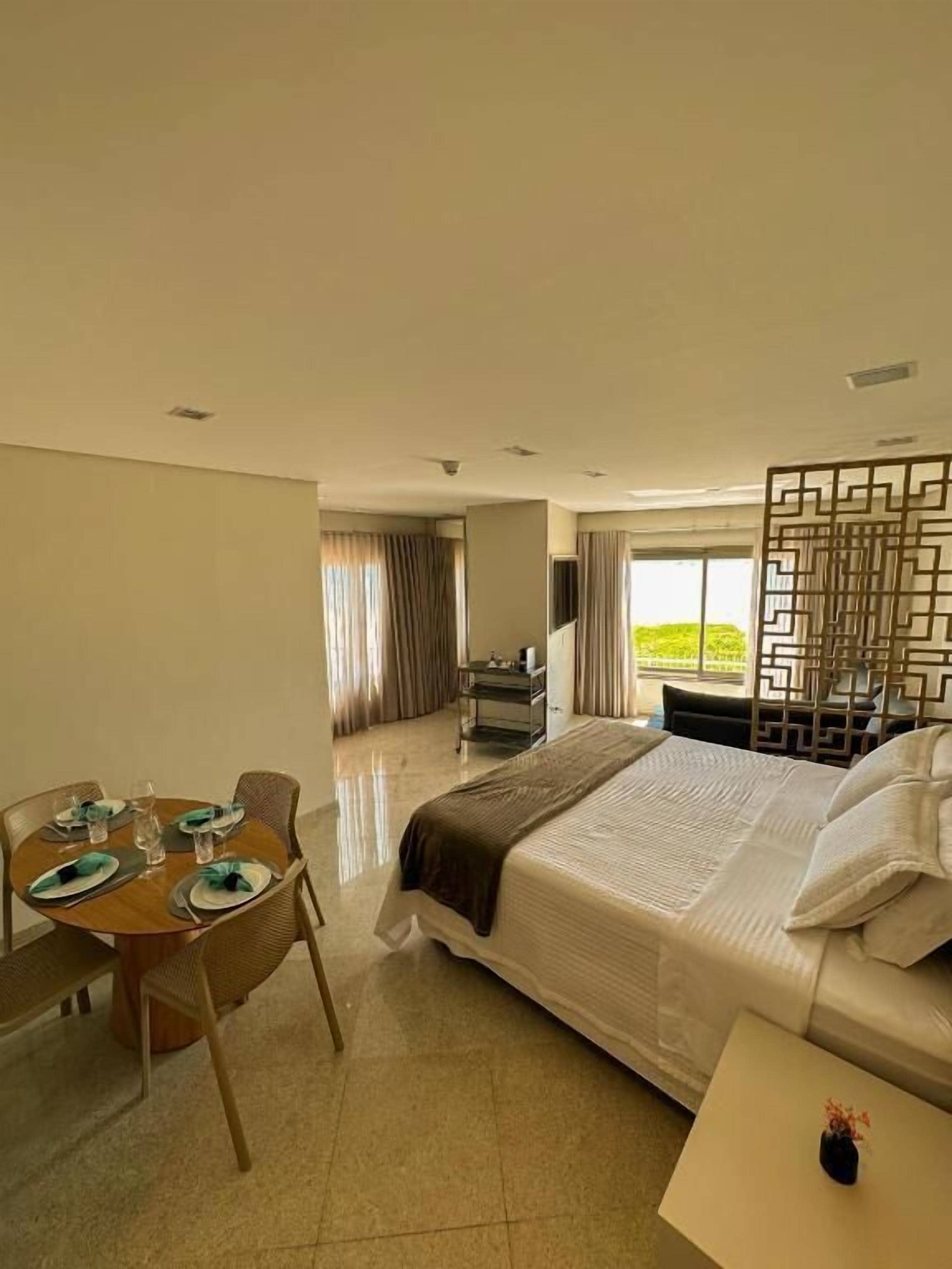 Habitación de hotel con cama, una mesa de comedor preparada para cuatro personas, un sofá y vistas a zonas verdes.