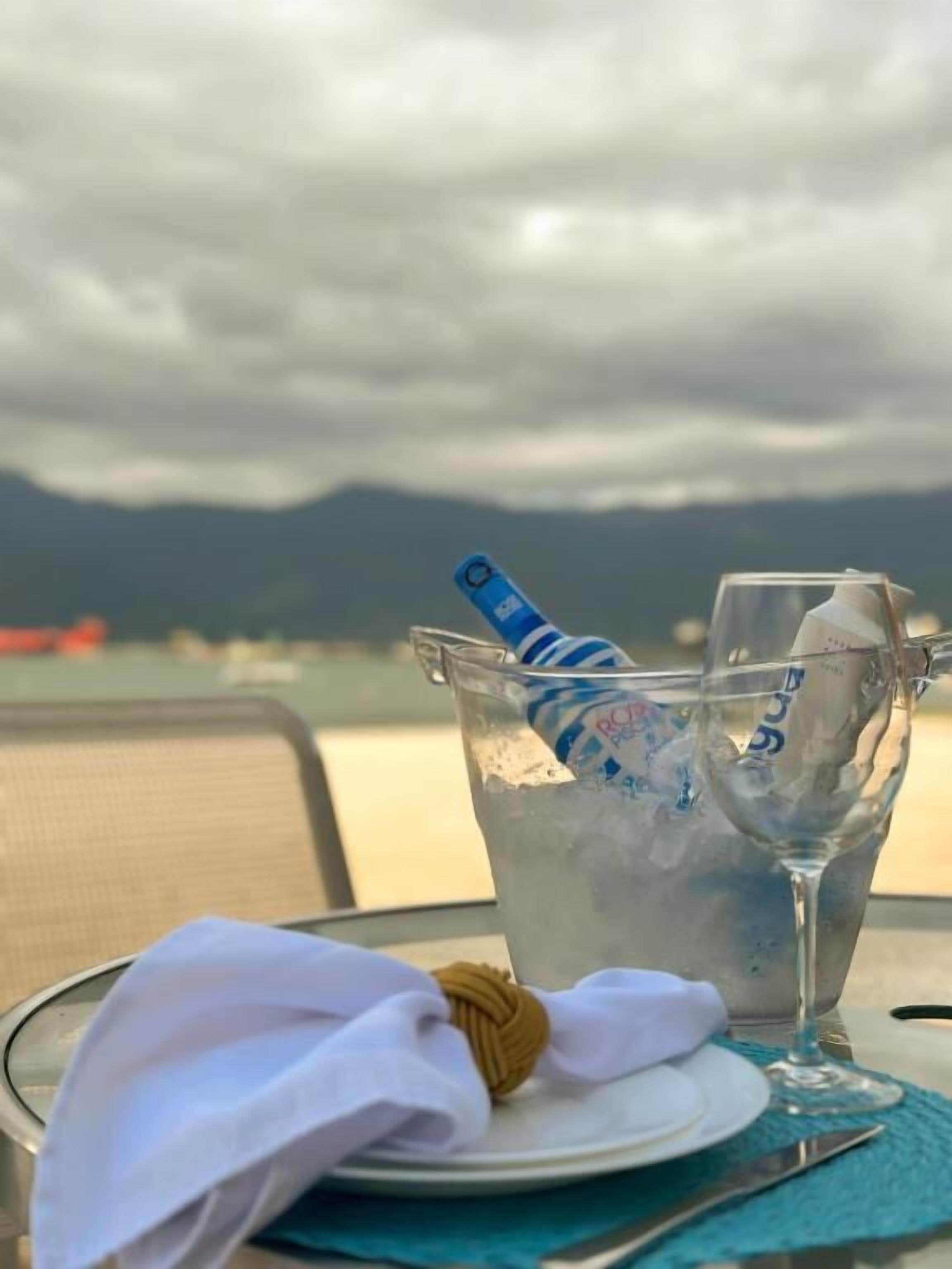 A table with a glass of water, a glass of ice, and a bottle of water, with a view of mountains and a cloudy sky in the background.