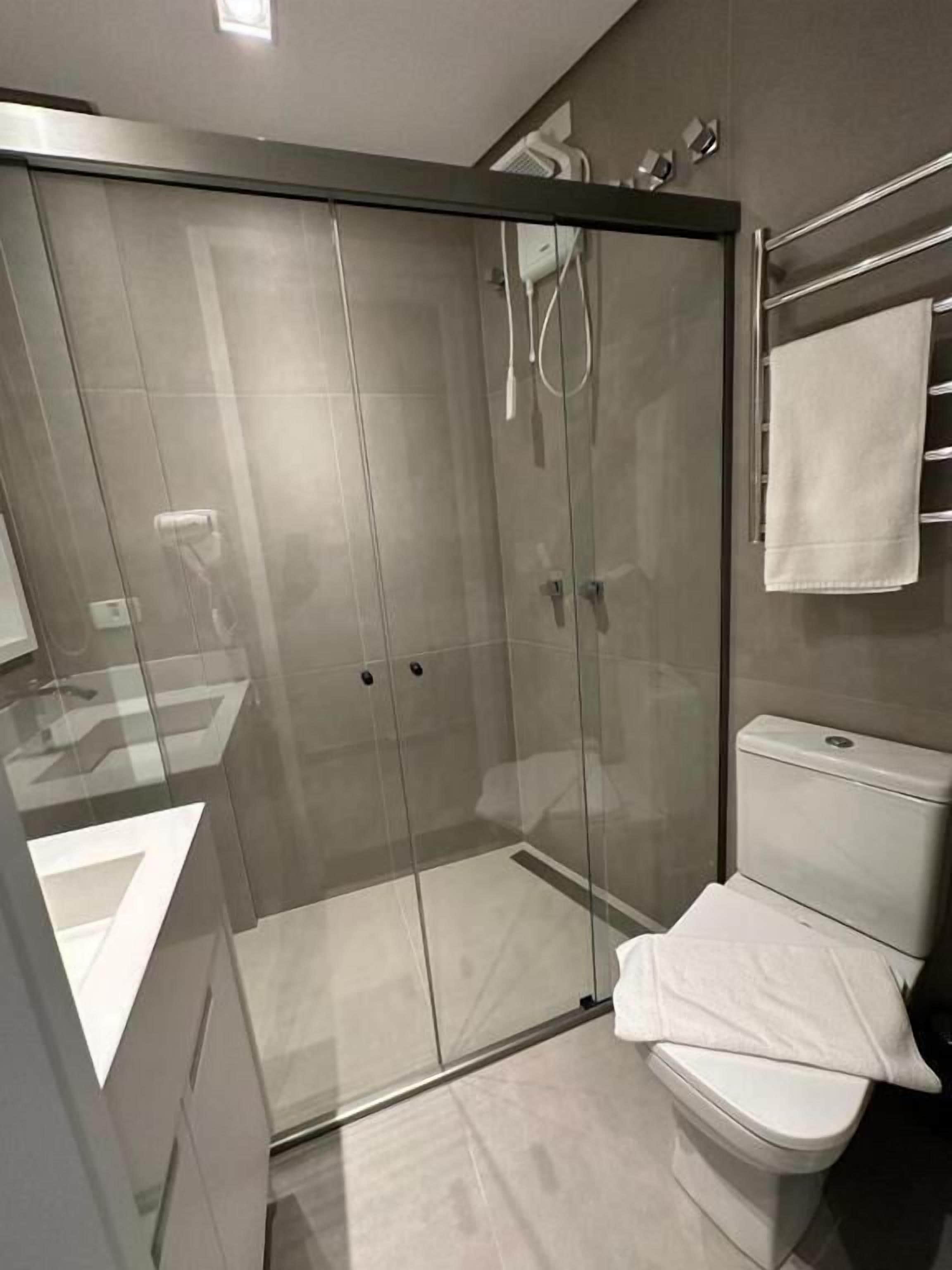 A modern bathroom with a glass-enclosed shower, a white toilet, and a towel rack.