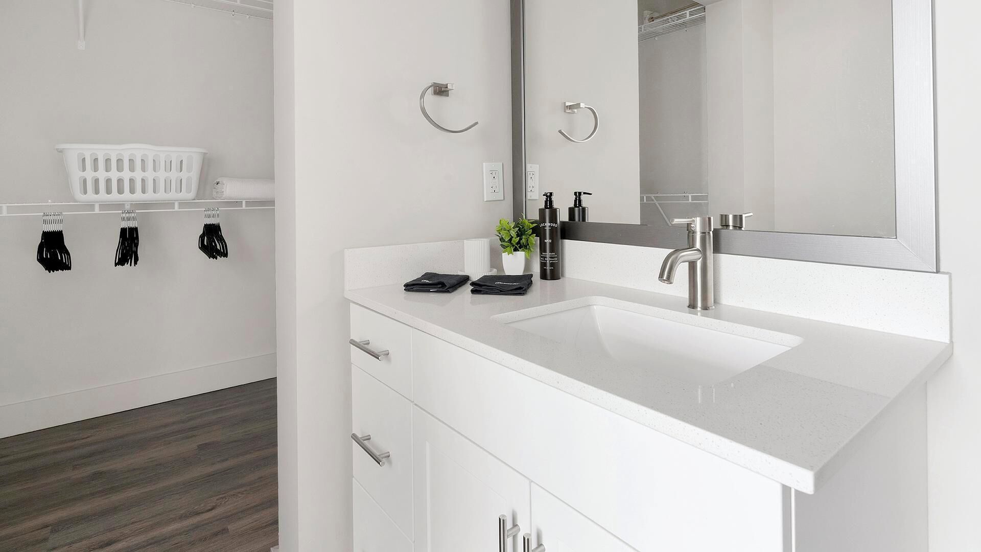 A modern bathroom with a white sink, a large mirror, and a white laundry basket.
