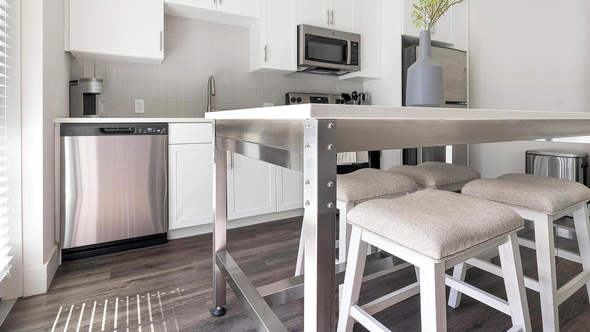 Une cuisine moderne avec des meubles blancs, des appareils en acier inoxydable et un îlot central doté de tabourets.