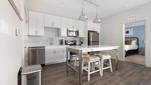 A modern kitchen with white cabinets, stainless steel appliances, and a central island with stools. - Landing | Modern 2BD, Gym (Fort Myers)