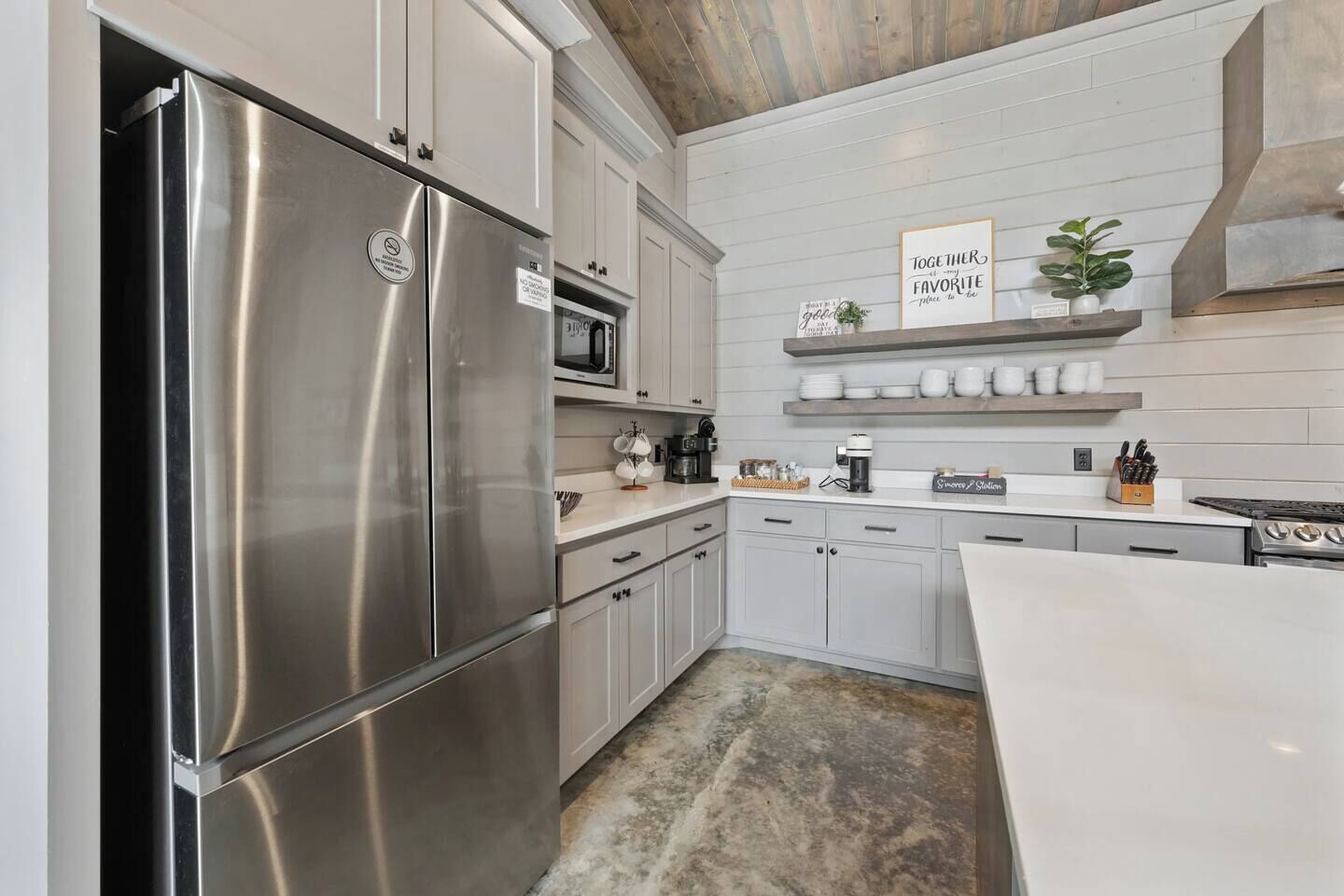 A modern kitchen with stainless steel appliances, white cabinetry, and a wooden ceiling.